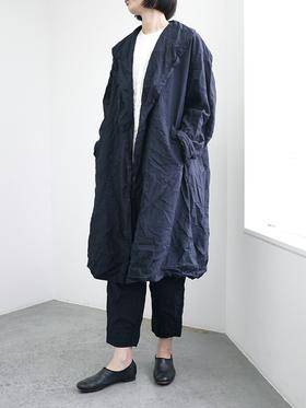 A woman wearing an oversized navy garment-dyed DDUD coat over a white tee and cropped black trousers