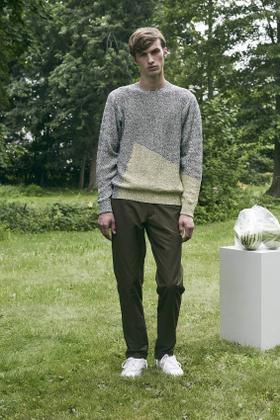 A man wearing a grey colour-blocked DDUGOFF sweater with brown trousers