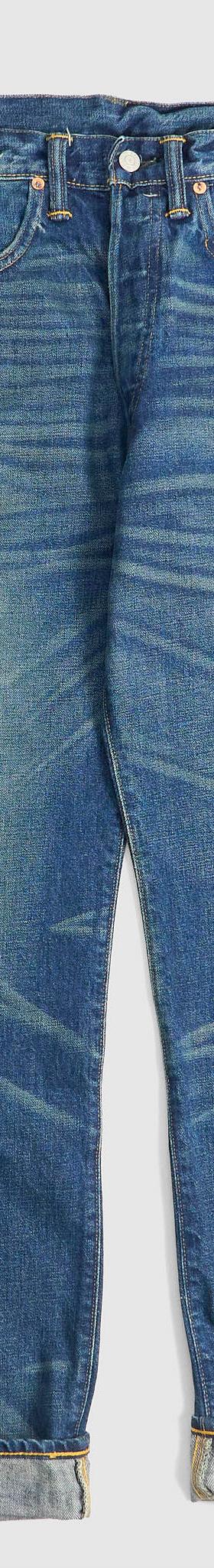 A pair of washed selvedge denim jeans with cuffed hems on a plain grey background