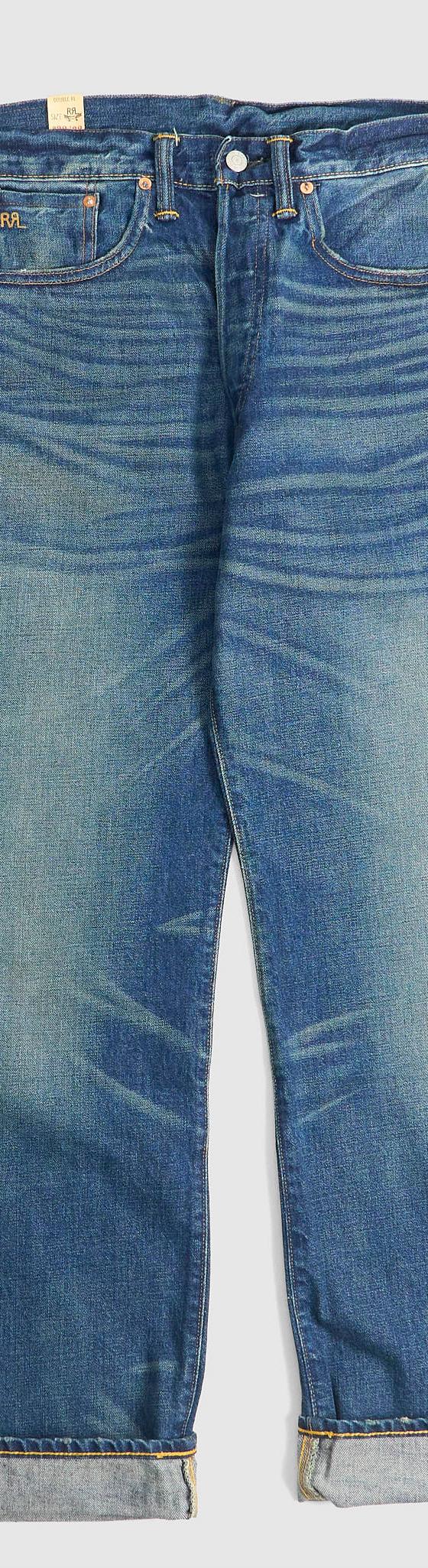 A pair of washed selvedge denim jeans with cuffed hems on a plain grey background