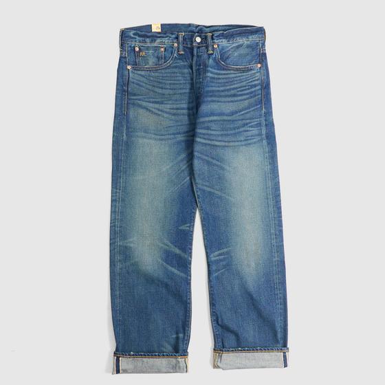 A pair of washed selvedge denim jeans with cuffed hems on a plain grey background