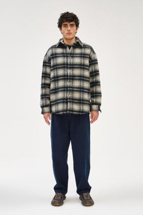 A man wearing a checked wool Delikatessen overshirt with navy relaxed trousers