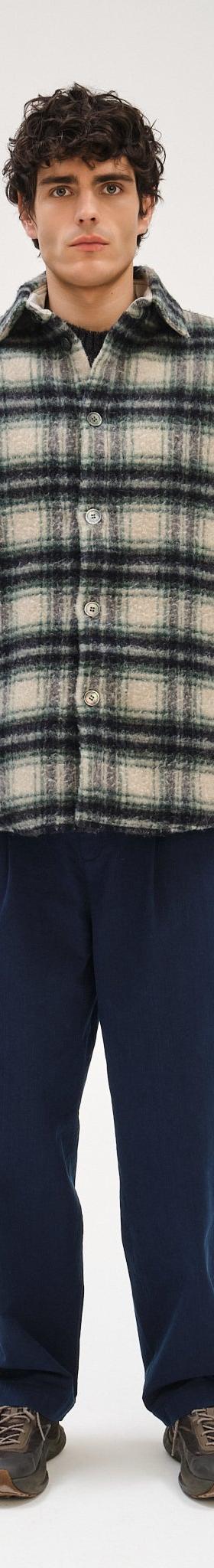 A man wearing a checked wool Delikatessen overshirt with navy relaxed trousers