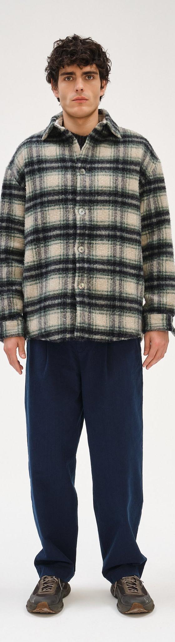 A man wearing a checked wool Delikatessen overshirt with navy relaxed trousers