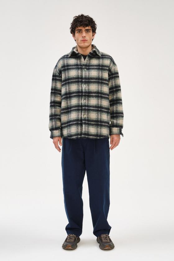 A man wearing a checked wool Delikatessen overshirt with navy relaxed trousers