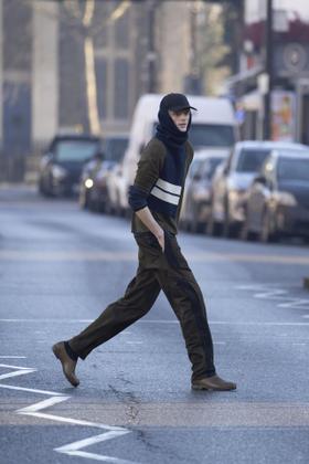 A man crossing a London street wearing a brown Derrick jacket and trousers with a navy striped knit scarf and cap