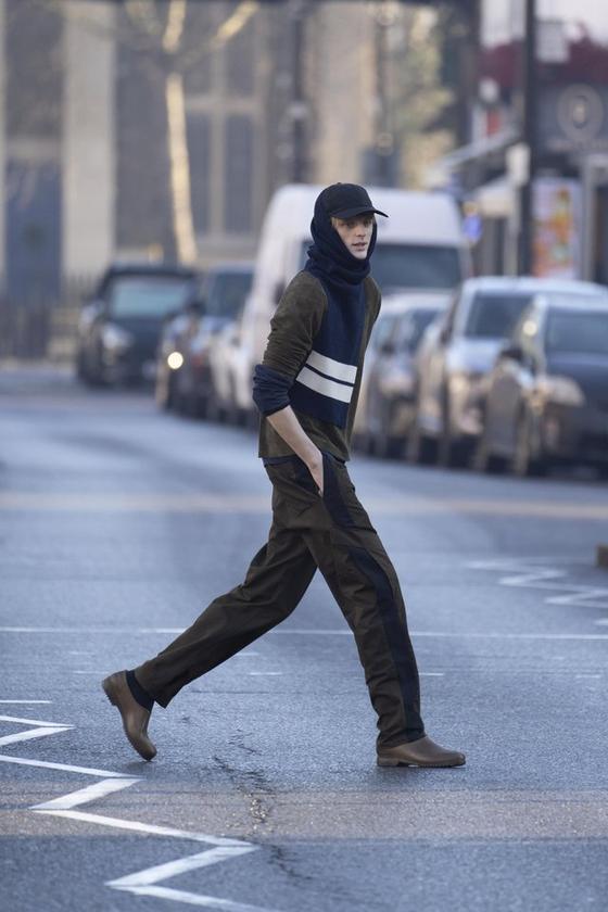 A man crossing a London street wearing a brown Derrick jacket and trousers with a navy striped knit scarf and cap