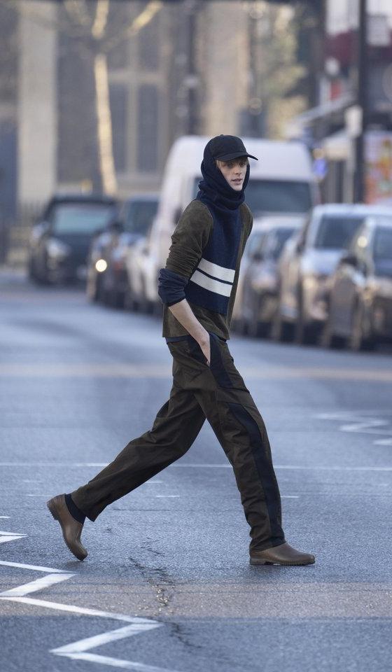 A man crossing a London street wearing a brown Derrick jacket and trousers with a navy striped knit scarf and cap