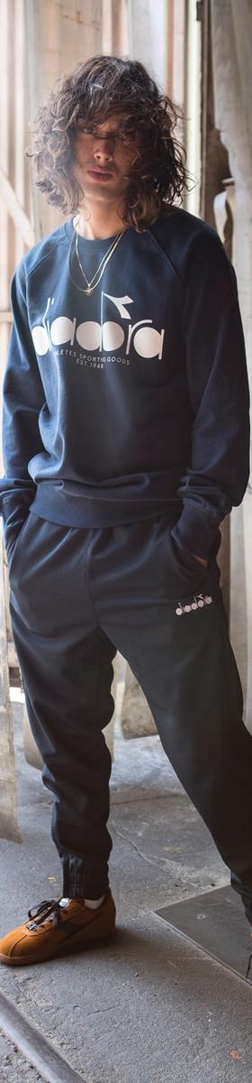 A man wearing a navy Diadora sweatshirt and matching track pants with tan suede sneakers