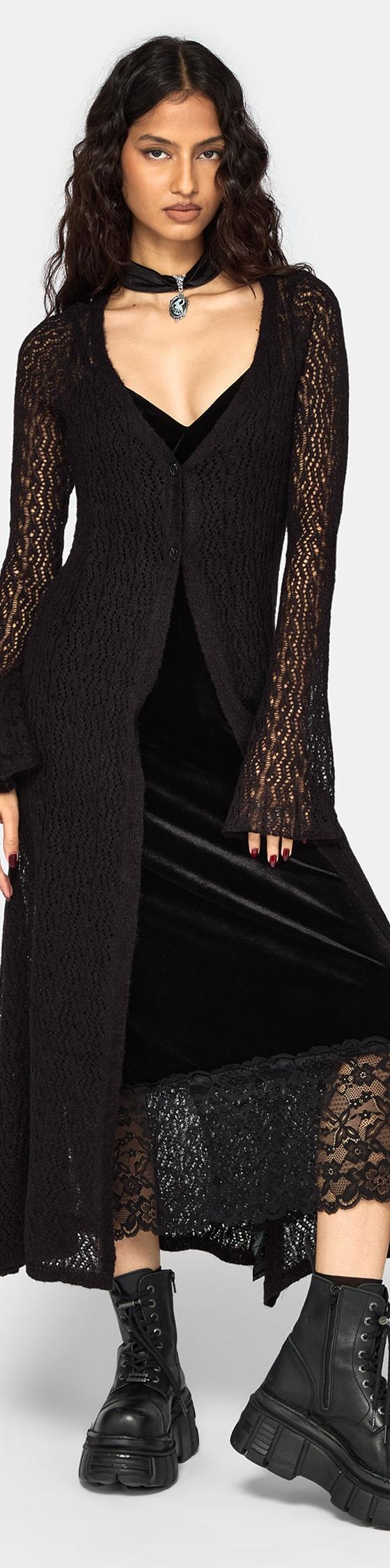 A woman wearing a black velvet lace-trim slip dress with a sheer knit longline cardigan and chunky platform boots