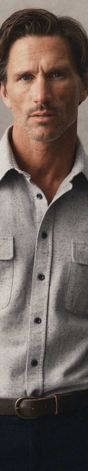 A man wearing a grey donegal flannel overshirt with navy trousers