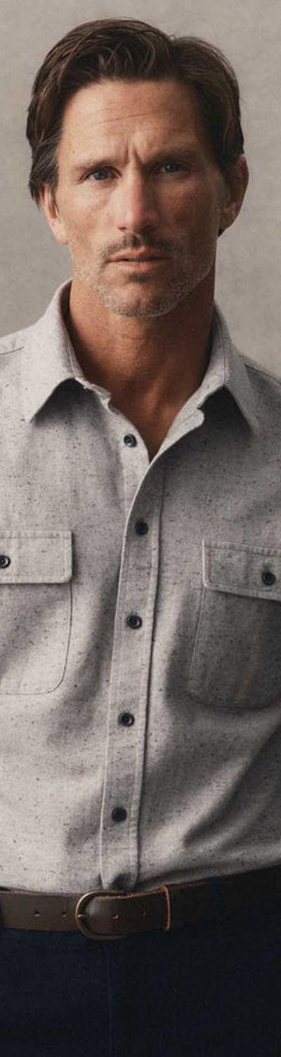 A man wearing a grey donegal flannel overshirt with navy trousers