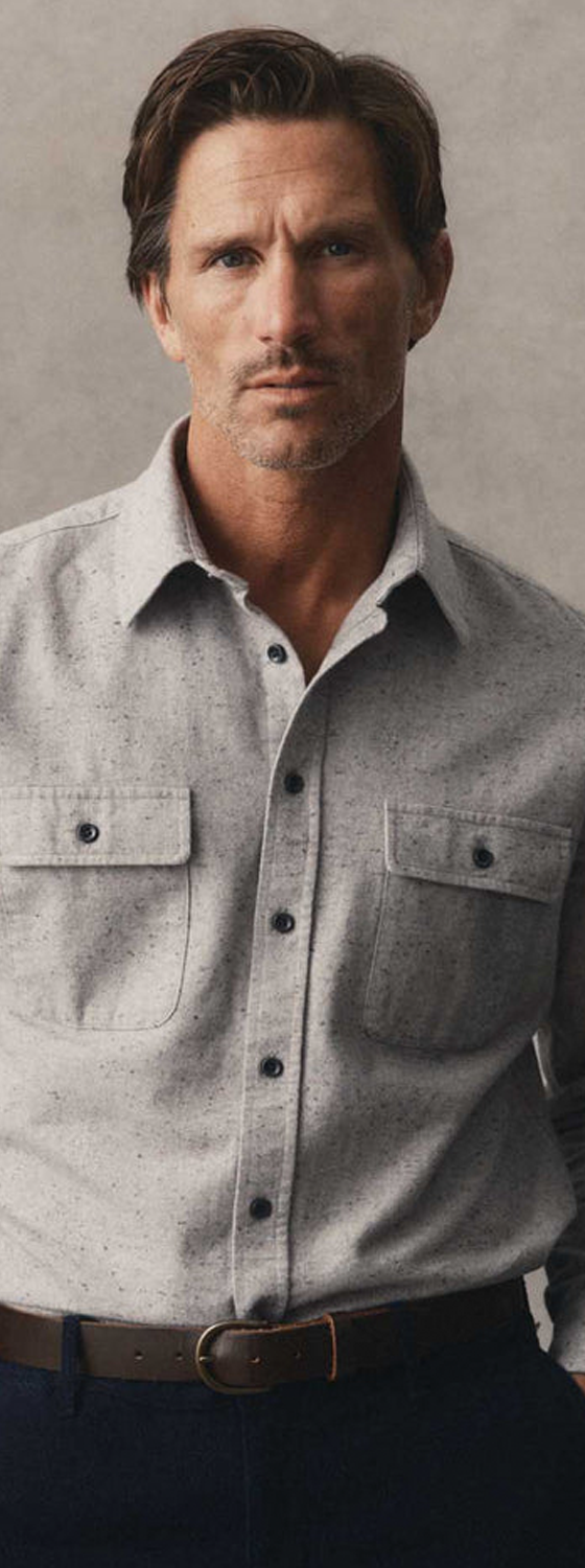A man wearing a grey donegal flannel overshirt with navy trousers