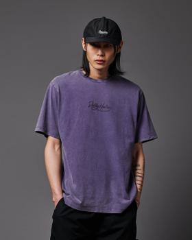 A man wearing a purple washed Dolly Noire script logo t-shirt and a black cap