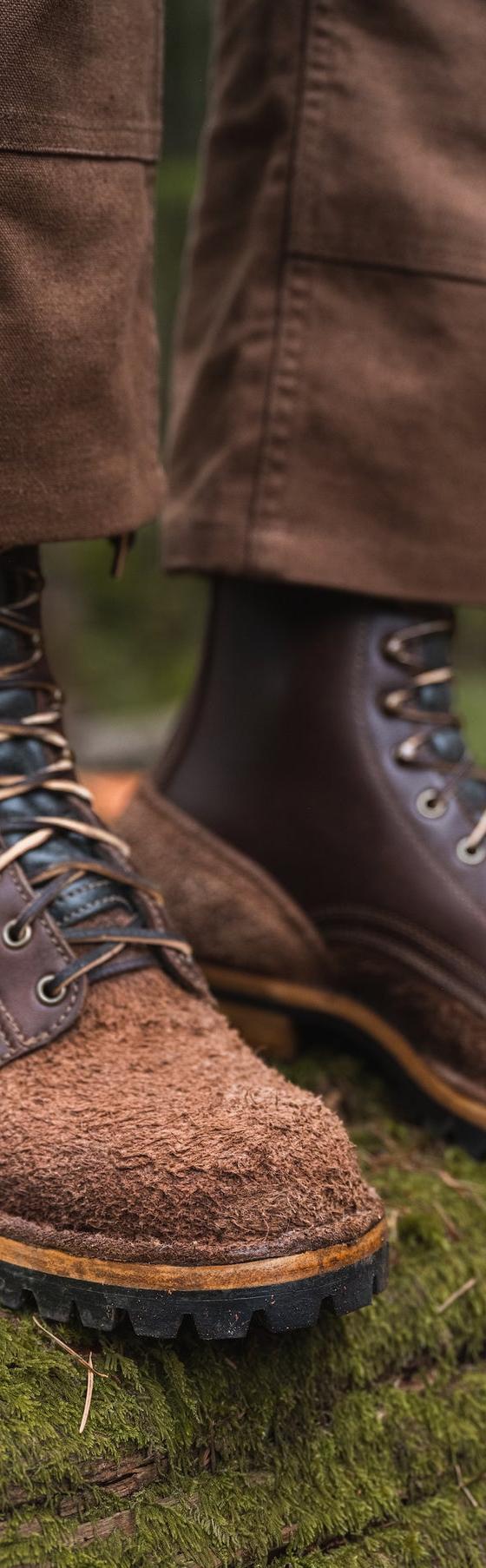 A man wearing brown roughout leather Drew's logger boots and waxed canvas trousers, standing on a mossy log in an Oregon forest
