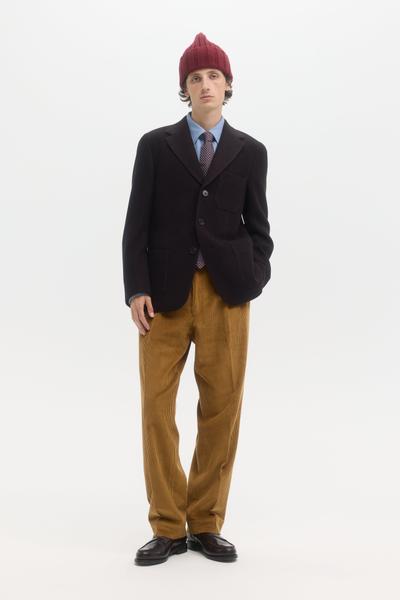 A man wearing a dark textured École de Pensée sport coat with tan corduroy trousers and a burgundy beanie