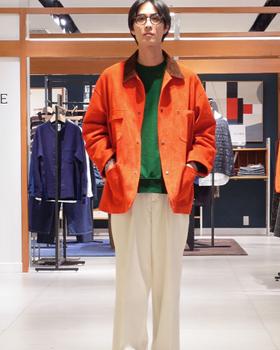 Staff member in an orange chore jacket inside an EDIFICE store, with racks and EDIFICE wall signage behind