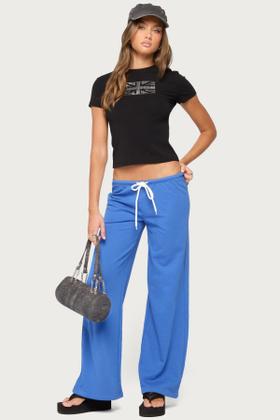 A woman wearing a black baby tee and blue low-rise wide-leg sweatpants with platform flip-flops