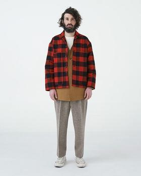 A man wearing a red buffalo check EEL Products overshirt with a tan tunic and flecked wool trousers