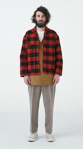 A man wearing a red buffalo check EEL Products overshirt with a tan tunic and flecked wool trousers