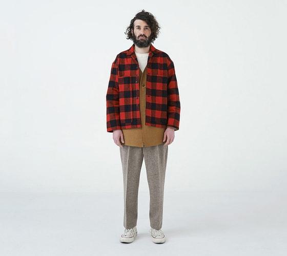 A man wearing a red buffalo check EEL Products overshirt with a tan tunic and flecked wool trousers