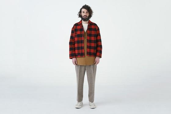 A man wearing a red buffalo check EEL Products overshirt with a tan tunic and flecked wool trousers
