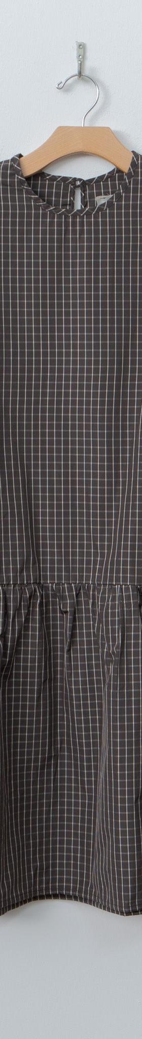 A brown checked ELEPH smock dress with gathered waist on a wooden hanger