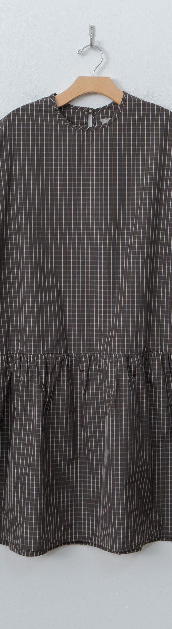 A brown checked ELEPH smock dress with gathered waist on a wooden hanger