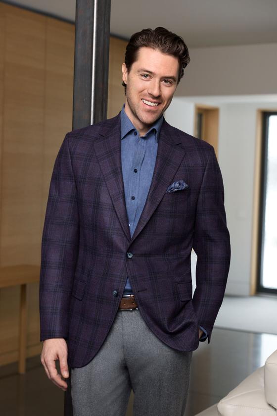 A man wearing a purple plaid Empire Clothing sport coat with a chambray shirt and grey flannel trousers
