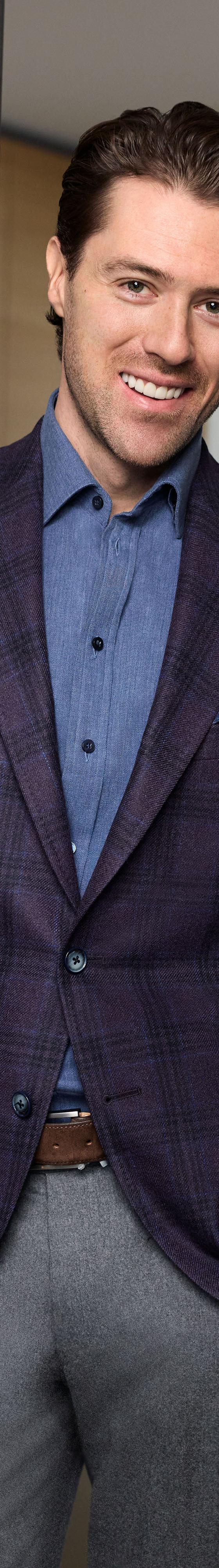 A man wearing a purple plaid Empire Clothing sport coat with a chambray shirt and grey flannel trousers