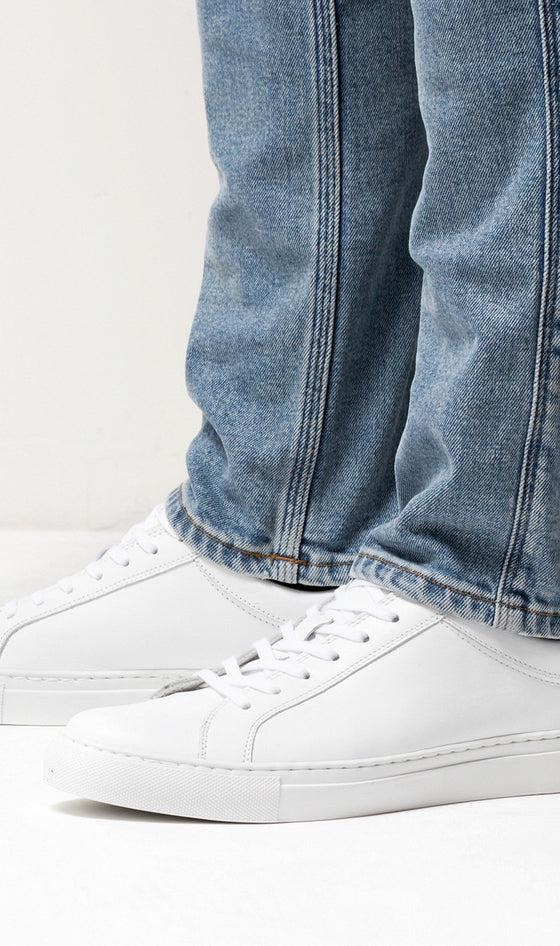 A man wearing white Erik Schedin leather sneakers with blue jeans