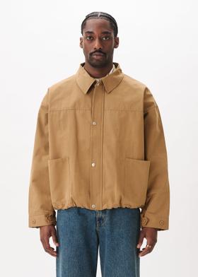 A man wearing a tan Estudio Niksen workwear jacket with blue jeans