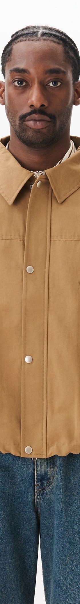 A man wearing a tan Estudio Niksen workwear jacket with blue jeans