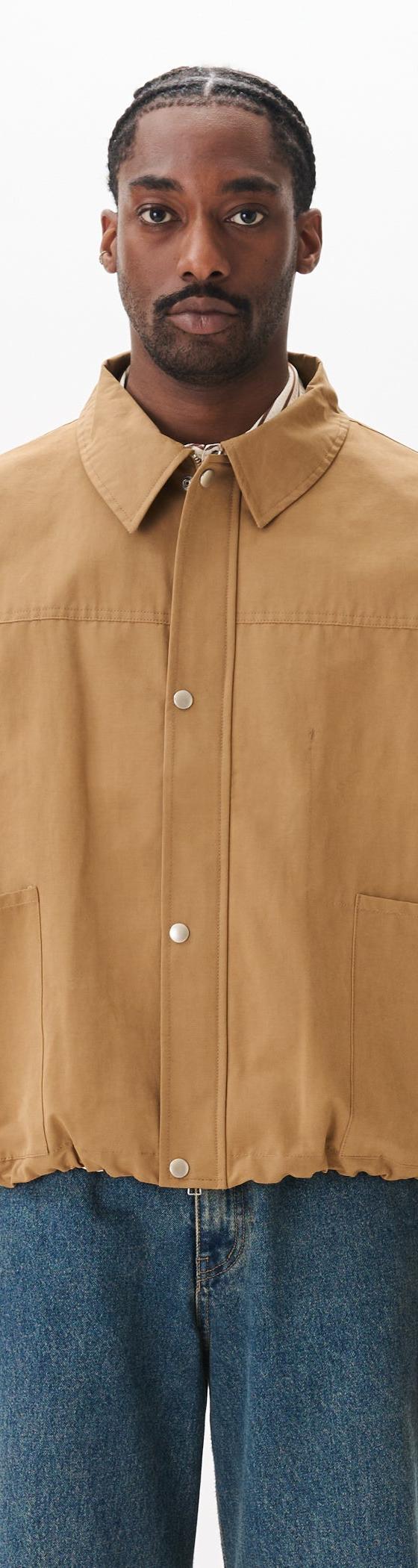 A man wearing a tan Estudio Niksen workwear jacket with blue jeans