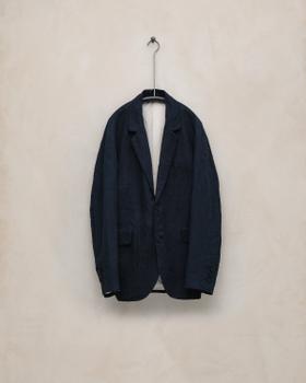 A navy linen tailored jacket by Evan Kinori hanging against a plaster wall
