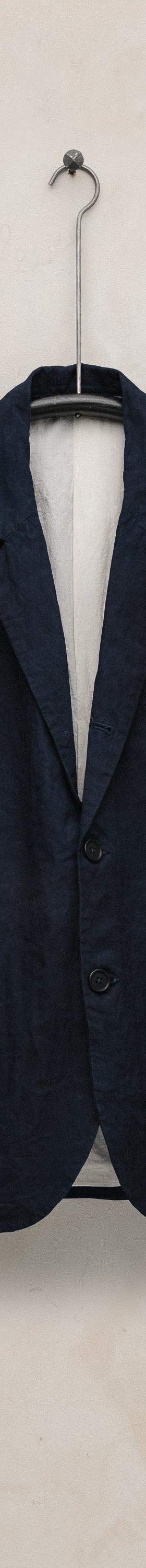 A navy linen tailored jacket by Evan Kinori hanging against a plaster wall
