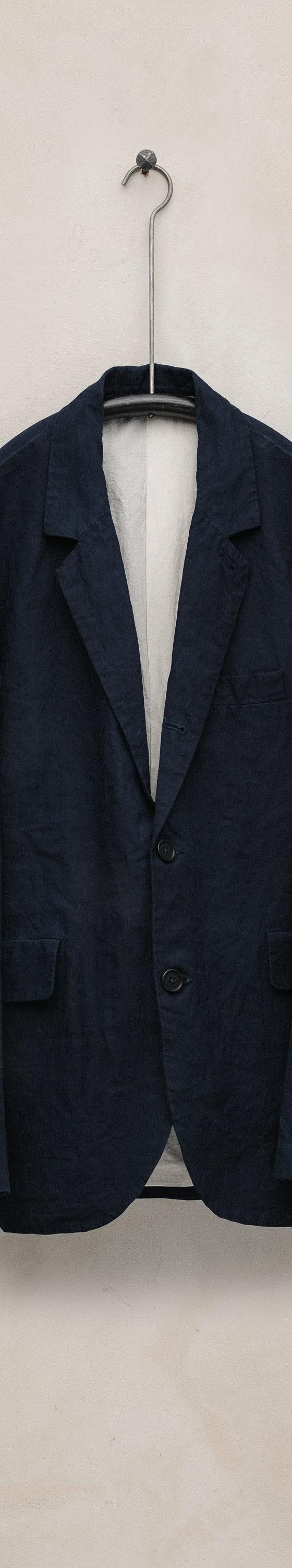 A navy linen tailored jacket by Evan Kinori hanging against a plaster wall
