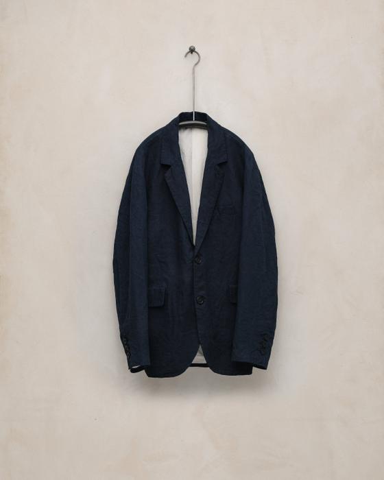 A navy linen tailored jacket by Evan Kinori hanging against a plaster wall