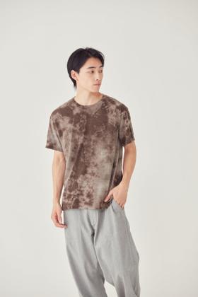 A man wearing a brown tie-dye FilMelange t-shirt with grey trousers