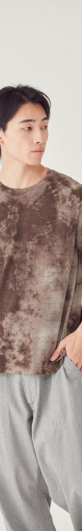 A man wearing a brown tie-dye FilMelange t-shirt with grey trousers