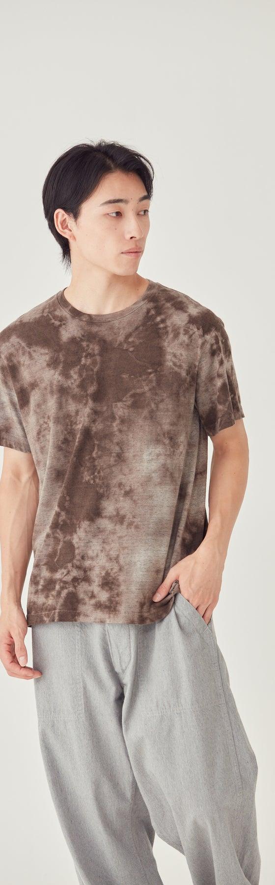 A man wearing a brown tie-dye FilMelange t-shirt with grey trousers