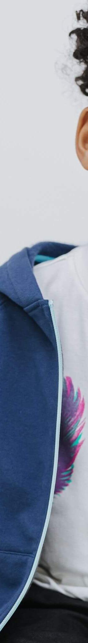 A young boy wearing a navy Firebird Kids zip-up hoodie over a feather-print tee