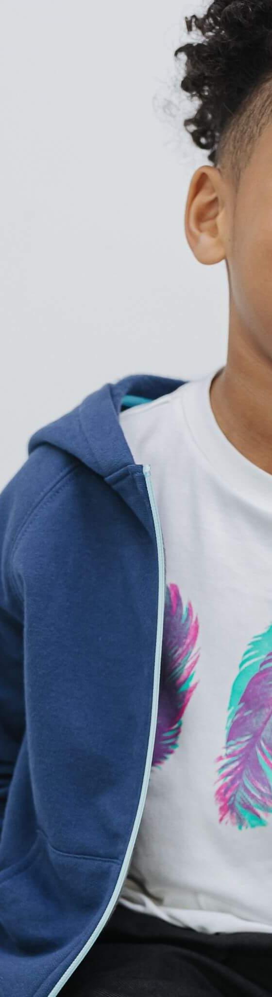 A young boy wearing a navy Firebird Kids zip-up hoodie over a feather-print tee