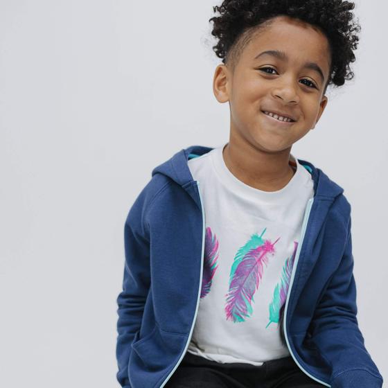 A young boy wearing a navy Firebird Kids zip-up hoodie over a feather-print tee