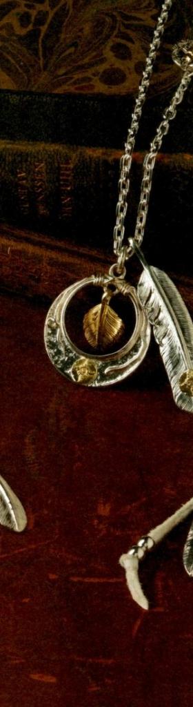 Silver feather pendants on fine chains, one set with turquoise, arranged on a dark burgundy surface