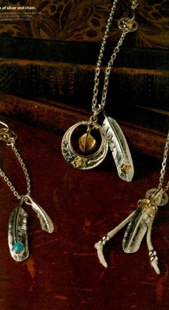 Silver feather pendants on fine chains, one set with turquoise, arranged on a dark burgundy surface