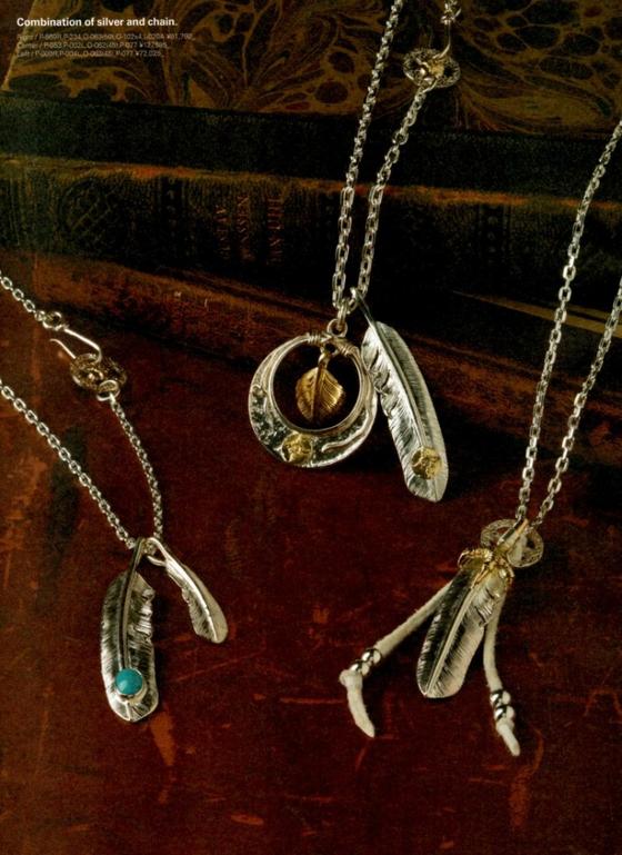 Silver feather pendants on fine chains, one set with turquoise, arranged on a dark burgundy surface