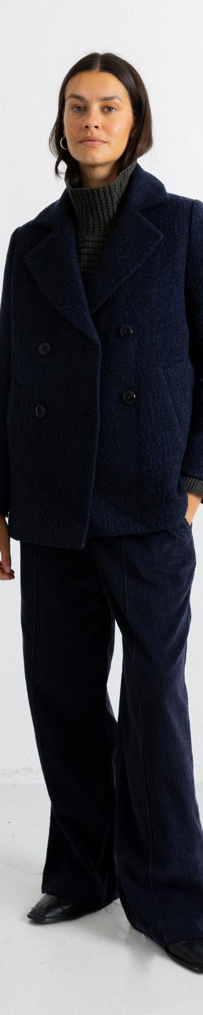 A woman wearing a navy textured wool Folk peacoat with matching wide-leg trousers