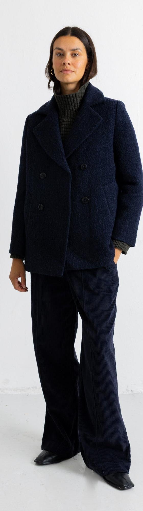 A woman wearing a navy textured wool Folk peacoat with matching wide-leg trousers