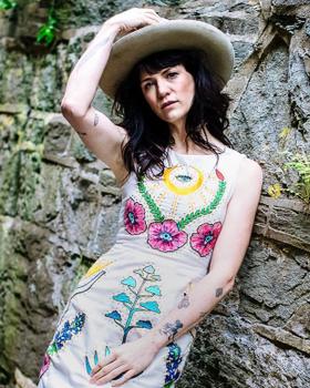 A woman in a wide-brim hat wearing a cream Fort Lonesome dress with colorful chainstitch floral embroidery